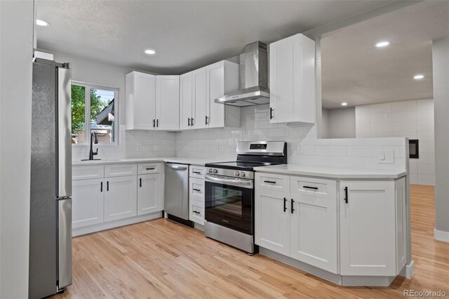 kitchen featuring appliances with stainless steel finishes, wall chimney exhaust hood, light hardwood / wood-style floors, and white cabinets