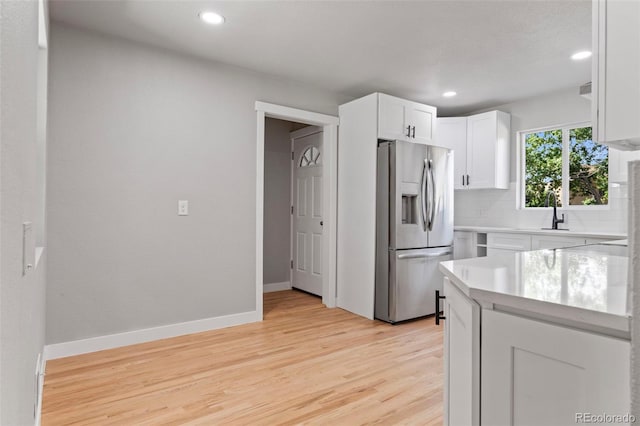 kitchen with sink, white cabinetry, light wood-type flooring, stainless steel fridge, and backsplash