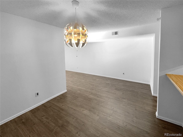 unfurnished dining area featuring a textured ceiling, dark wood-type flooring, and an inviting chandelier