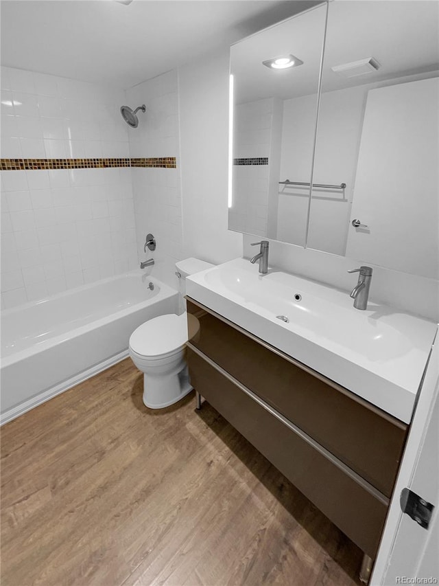 full bathroom featuring toilet, hardwood / wood-style flooring, tiled shower / bath combo, and vanity