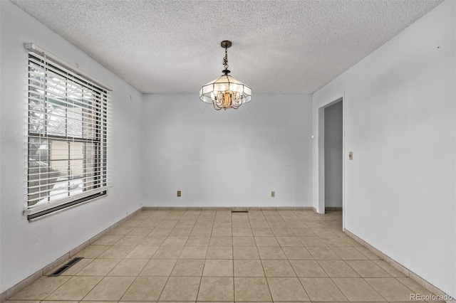 tiled spare room featuring an inviting chandelier and a textured ceiling