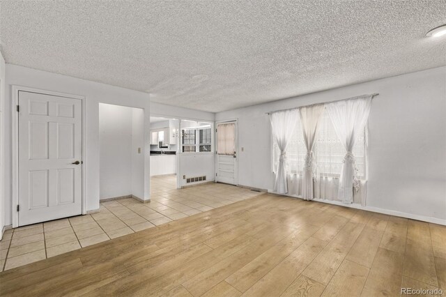 unfurnished living room featuring a textured ceiling, visible vents, baseboards, and wood finished floors