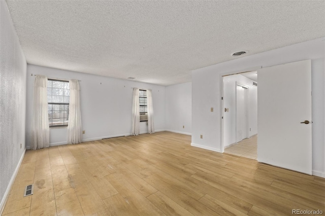 empty room with baseboards, light wood-style flooring, a textured ceiling, and visible vents