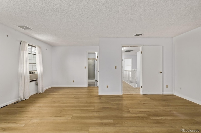 spare room featuring light wood-style floors, baseboards, a textured ceiling, and visible vents