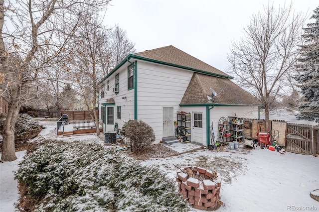 snow covered house with a fenced backyard, cooling unit, an outdoor fire pit, and roof with shingles