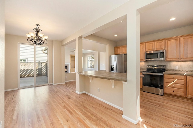 kitchen featuring pendant lighting, light hardwood / wood-style flooring, appliances with stainless steel finishes, tasteful backsplash, and a kitchen bar