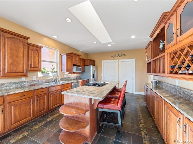 kitchen featuring stainless steel appliances, light stone counters, a kitchen island, sink, and a breakfast bar area