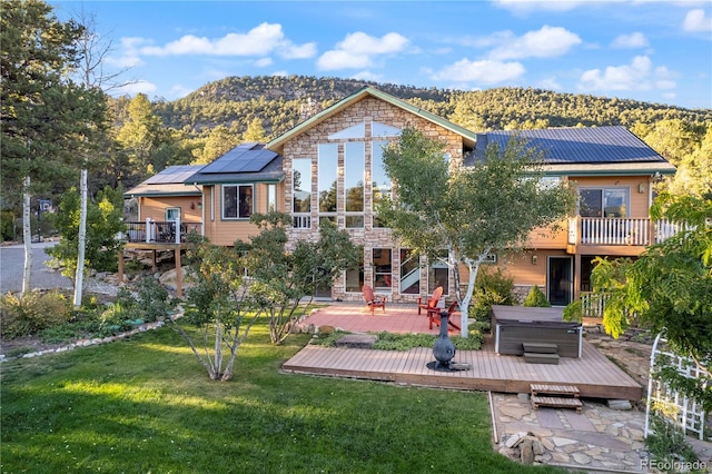 rear view of property featuring a yard, solar panels, a deck with mountain view, and a hot tub