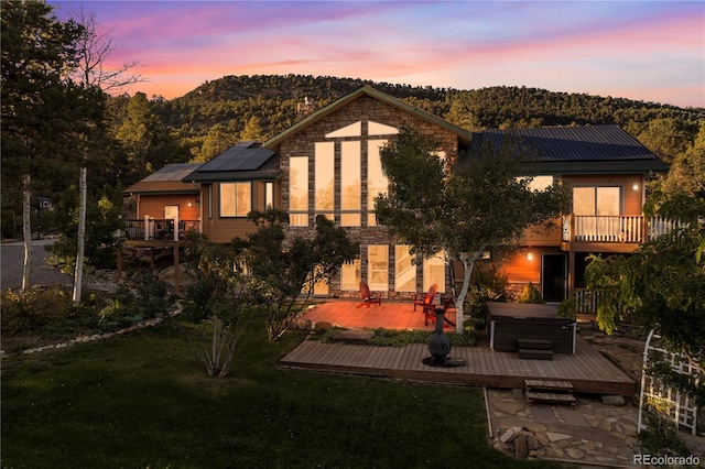 back house at dusk featuring a jacuzzi, a yard, a patio, and a deck