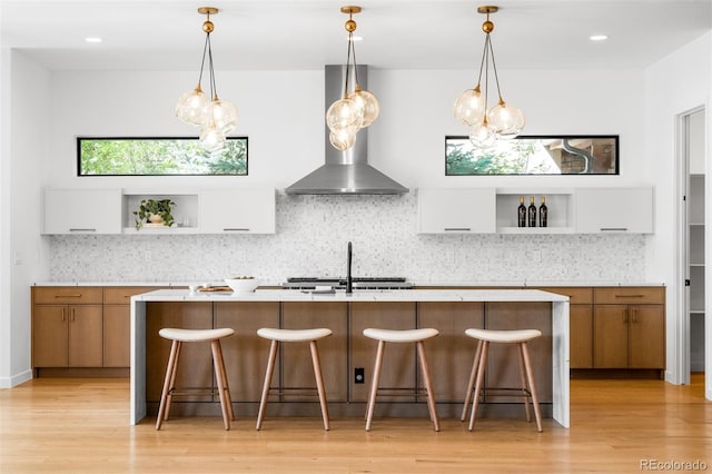 kitchen featuring open shelves, wall chimney exhaust hood, light countertops, light wood finished floors, and recessed lighting