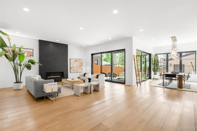 living area with light wood-style flooring, recessed lighting, a large fireplace, baseboards, and a chandelier