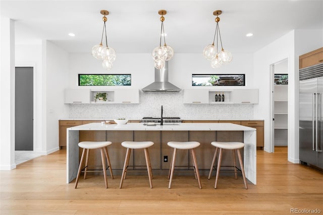 kitchen featuring built in refrigerator, wall chimney exhaust hood, open shelves, light wood-style flooring, and recessed lighting