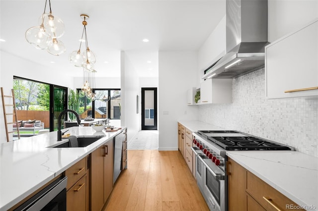 kitchen with stainless steel appliances, a sink, wall chimney range hood, a chandelier, and brown cabinetry
