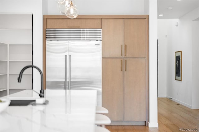 kitchen with built in refrigerator, light wood-style floors, light countertops, a sink, and baseboards