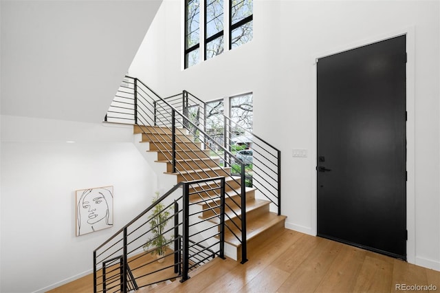 entryway featuring a towering ceiling, wood finished floors, baseboards, and stairs