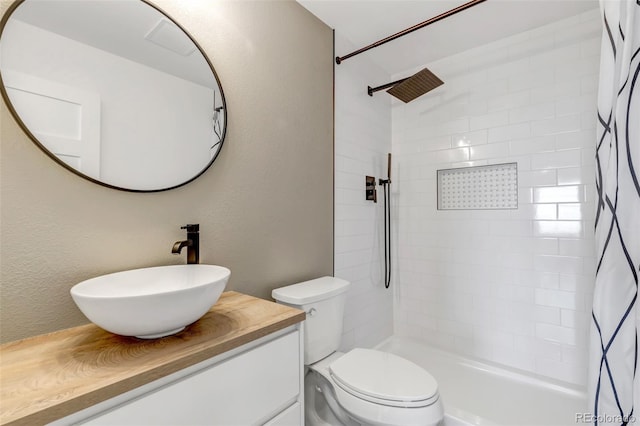 bathroom featuring toilet, a textured wall, tiled shower, and vanity