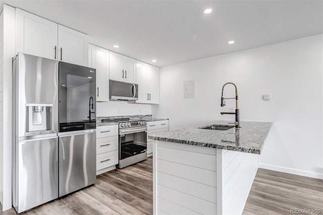 kitchen featuring stone counters, appliances with stainless steel finishes, light wood finished floors, and a sink