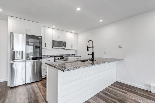 kitchen with stone counters, dark wood-style flooring, appliances with stainless steel finishes, a sink, and a peninsula