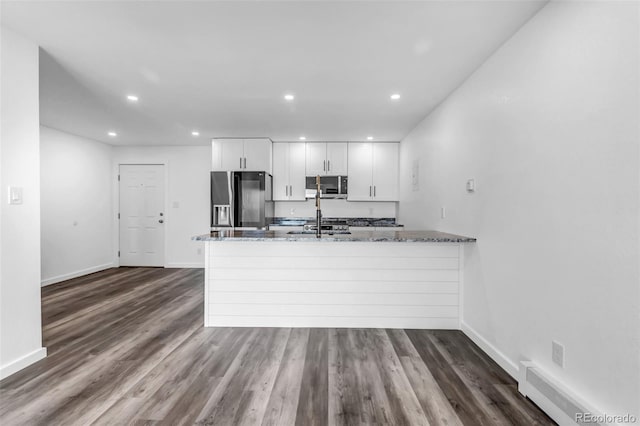 kitchen featuring dark wood finished floors, appliances with stainless steel finishes, a peninsula, stone counters, and white cabinetry