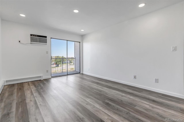 unfurnished room with baseboard heating, a wall mounted air conditioner, wood finished floors, and baseboards