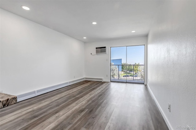 spare room with an AC wall unit, recessed lighting, wood finished floors, and baseboards