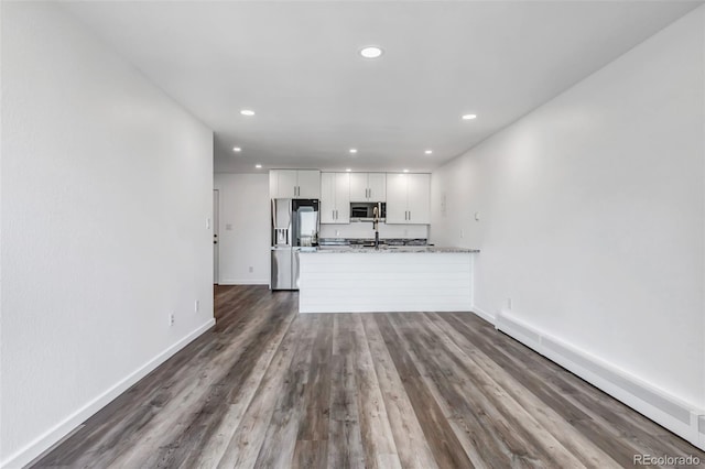 kitchen with stainless steel appliances, a peninsula, white cabinetry, baseboards, and baseboard heating