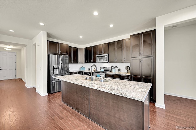 6335 E 143rd Dr, Thornton, CO 80602 - kitchen featuring appliances with stainless steel finishes, dark wood-style flooring, dark brown cabinets, light stone counters, and a center island with sink
