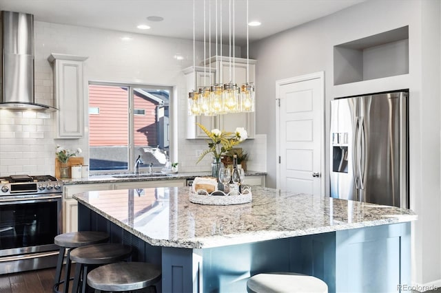 kitchen featuring a breakfast bar area, decorative light fixtures, a center island, appliances with stainless steel finishes, and wall chimney range hood