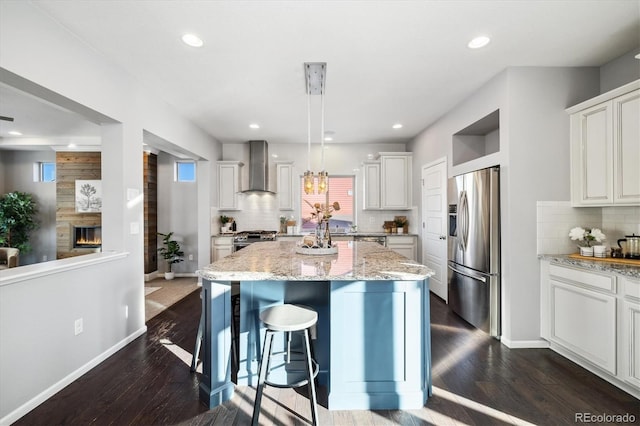 kitchen with stainless steel appliances, a center island, wall chimney range hood, and white cabinets