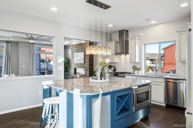 kitchen featuring white cabinetry, appliances with stainless steel finishes, a center island, and wall chimney range hood