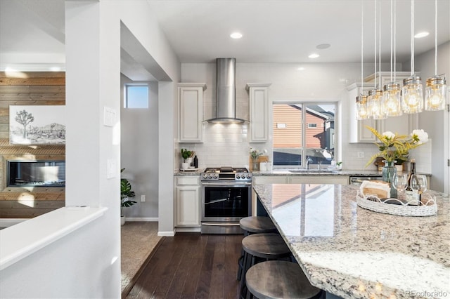 kitchen featuring pendant lighting, white cabinets, stainless steel range with gas stovetop, and wall chimney exhaust hood