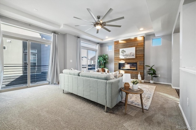 living room with light carpet, a tray ceiling, a fireplace, and ceiling fan