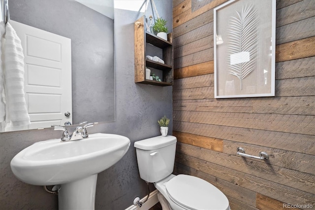 bathroom with toilet, wooden walls, and sink