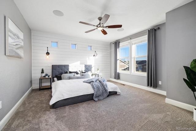 bedroom featuring dark colored carpet, wooden walls, and ceiling fan