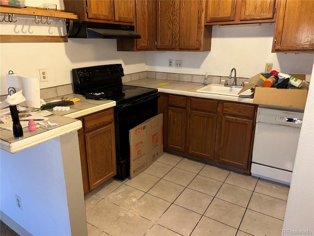 kitchen featuring tile counters, a sink, dishwasher, under cabinet range hood, and black / electric stove