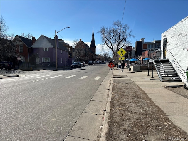 view of road featuring street lights, sidewalks, curbs, a residential view, and traffic signs