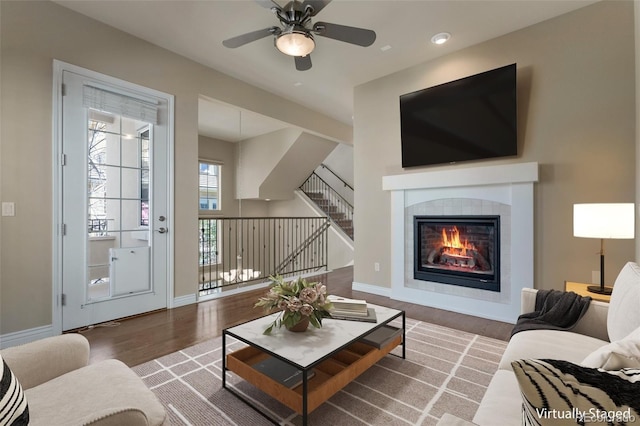 living room featuring ceiling fan, baseboards, stairway, a tile fireplace, and wood finished floors