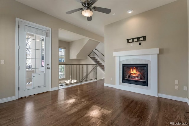 unfurnished living room with baseboards, a ceiling fan, wood finished floors, and a tiled fireplace