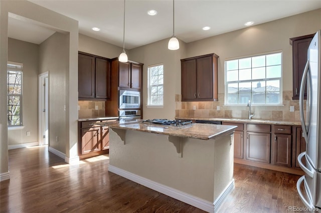 kitchen featuring light stone countertops, a kitchen island, dark wood finished floors, a sink, and stainless steel appliances