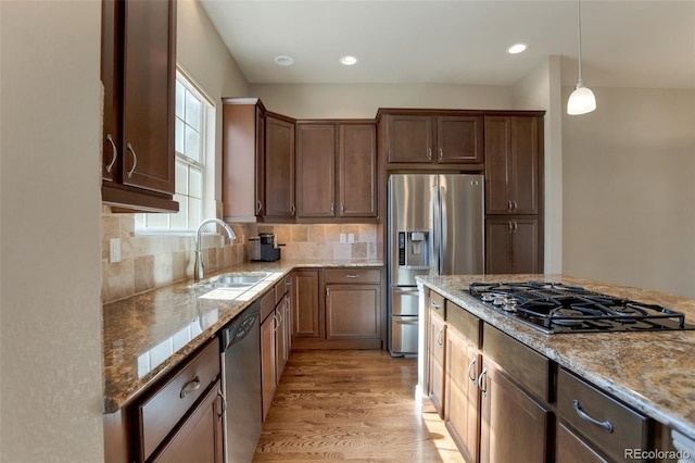 kitchen with light wood finished floors, light stone counters, decorative backsplash, stainless steel appliances, and a sink