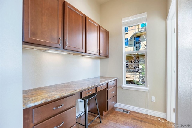 office area featuring visible vents, light wood finished floors, baseboards, and built in study area