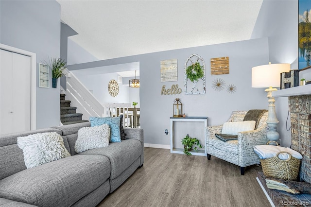 living area with wood finished floors, an inviting chandelier, baseboards, stairs, and vaulted ceiling