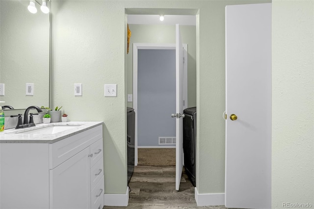 bathroom with visible vents, vanity, baseboards, and wood finished floors