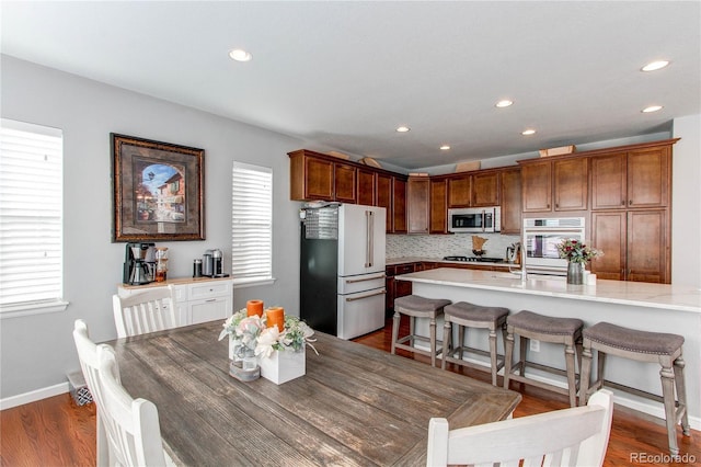 kitchen with sink, white appliances, dark wood-type flooring, backsplash, and a kitchen bar