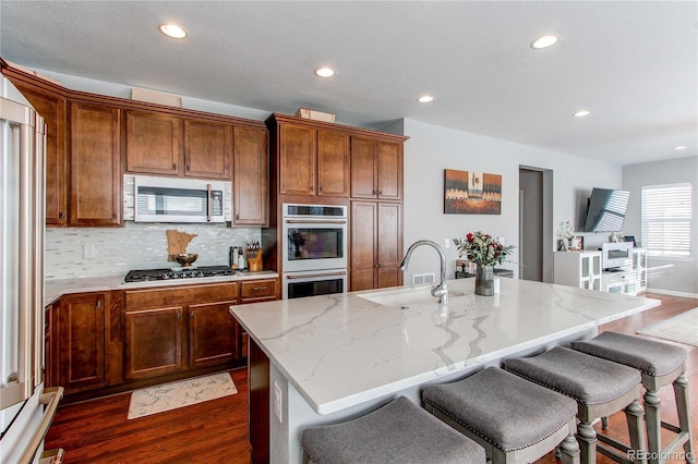 kitchen featuring sink, appliances with stainless steel finishes, an island with sink, a kitchen bar, and dark hardwood / wood-style flooring