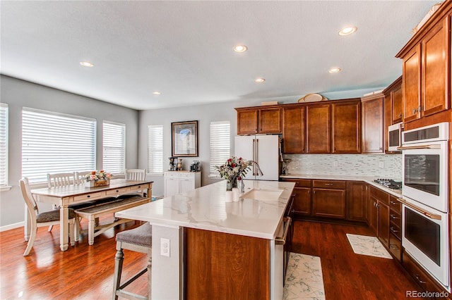 kitchen with sink, dark hardwood / wood-style flooring, decorative backsplash, a kitchen island with sink, and stainless steel appliances