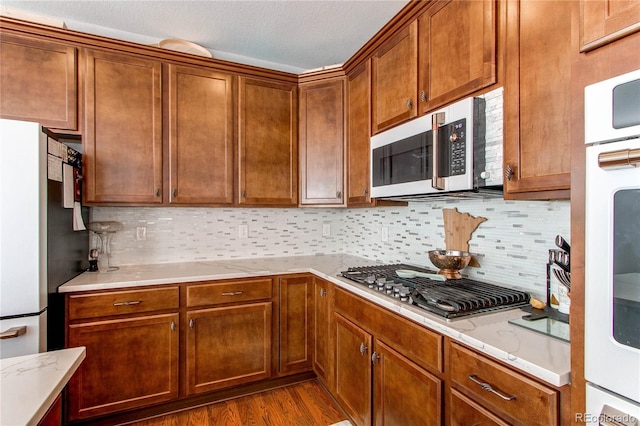 kitchen featuring stainless steel gas cooktop, light stone counters, fridge, hardwood / wood-style flooring, and decorative backsplash