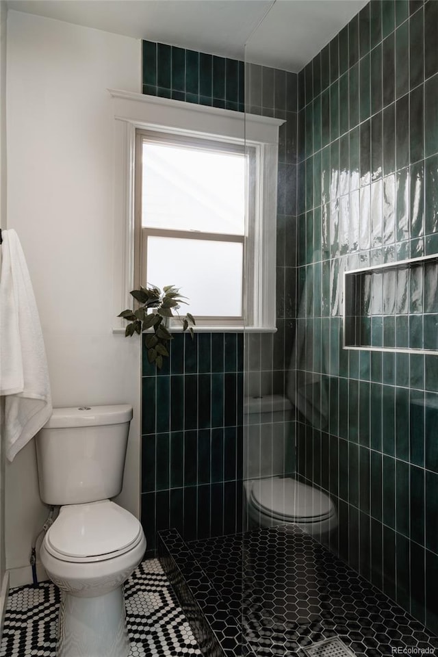 bathroom featuring tiled shower, tile patterned flooring, and toilet