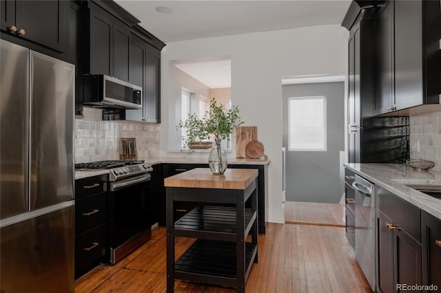 kitchen featuring appliances with stainless steel finishes, light wood-type flooring, tasteful backsplash, and plenty of natural light