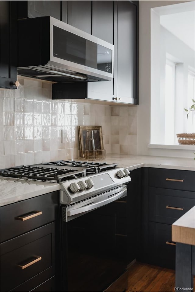 kitchen with decorative backsplash, dark hardwood / wood-style floors, light stone countertops, and appliances with stainless steel finishes